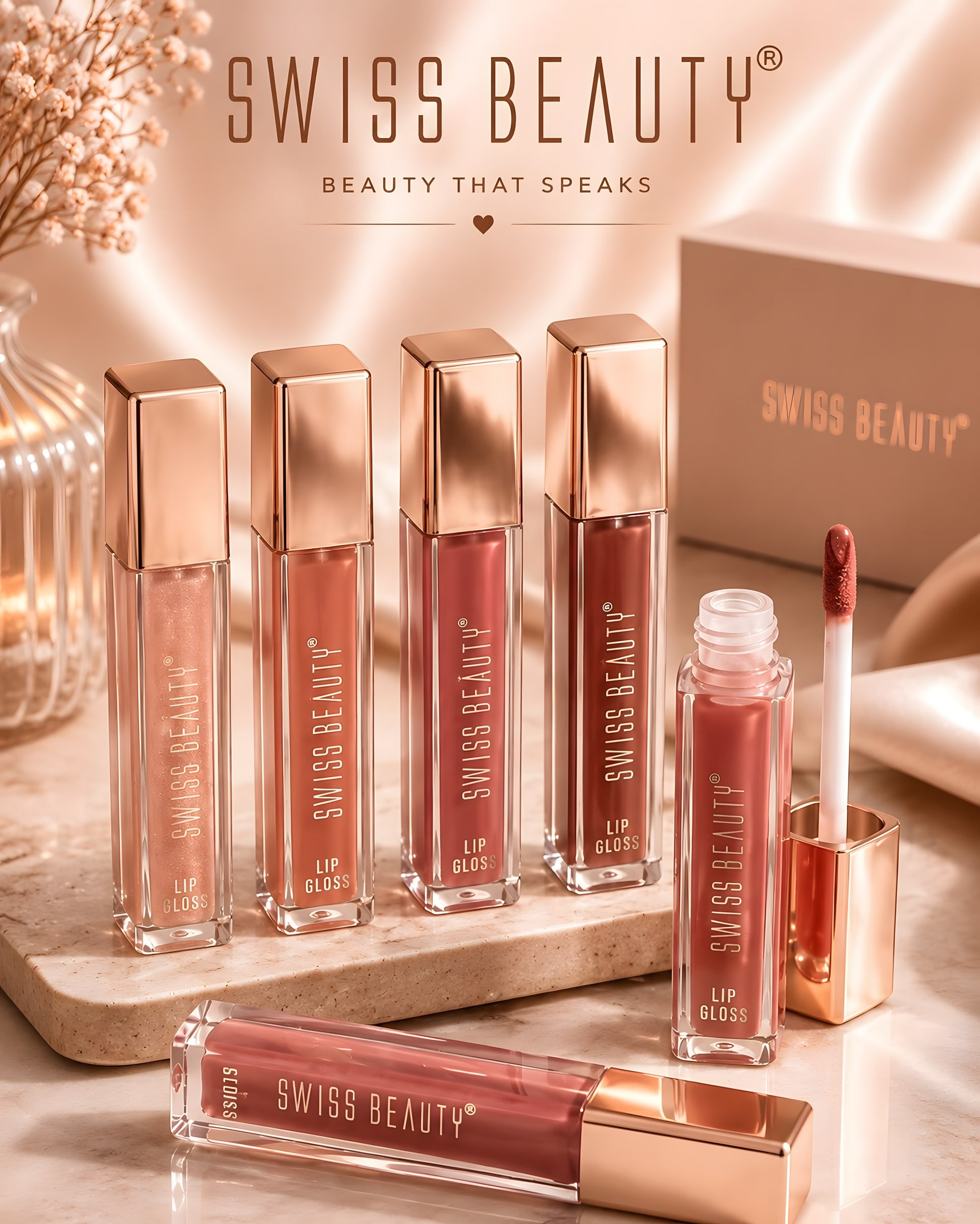 A row of Swiss Beauty lip glosses with rose-gold caps on a stone tray
